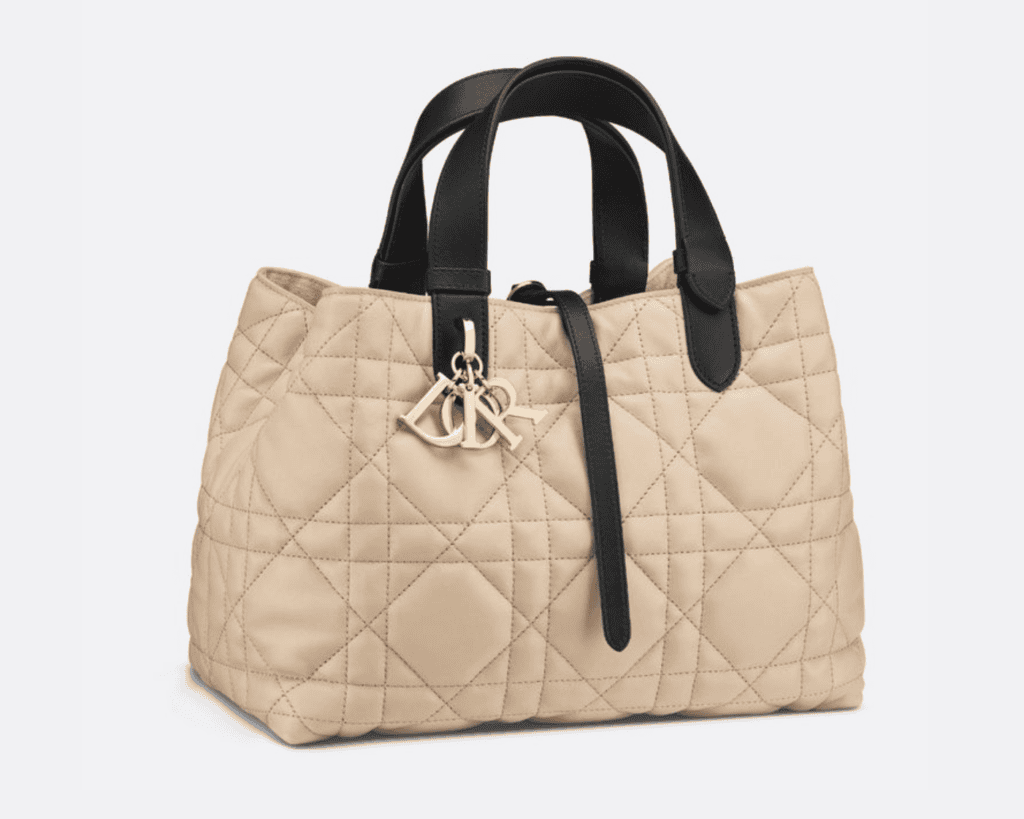 Medium Dior Toujours tote bag in powder beige Macrocannage quilted calfskin leather featuring contrasting black adjustable leather top handles, a crossover leather tie strap, and pale gold-finish D.I.O.R. charms.