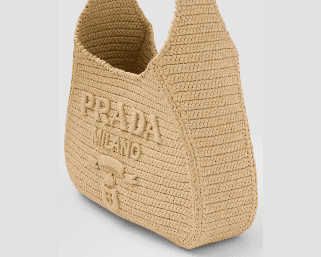 Prada crochet shoulder bag in natural beige raffia featuring an open hobo silhouette and an embroidered tonal PRADA MILANO lettering logo with a heritage coat of arms.