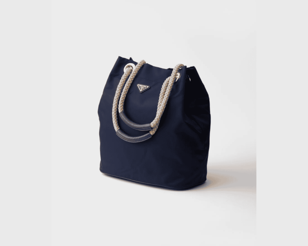 Prada Mariner bucket bag in Baltic blue Re-Nylon fabric featuring thick braided cream rope top handles with leather grip accents and the iconic silver-tone enameled metal triangle logo.