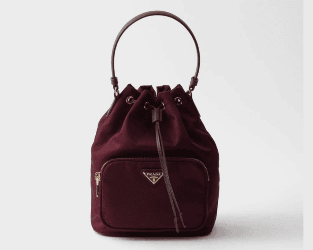 Prada Duet bucket bag in burgundy wine Re-Nylon fabric featuring a Saffiano leather top handle, drawstring closure, zippered front pocket, and silver-tone triangle logo.