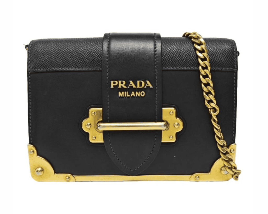 Prada Cahier shoulder bag in black smooth city calf and textured Saffiano leather featuring prominent gold-tone corner plates, a lock strap closure, and a gold curb chain strap.