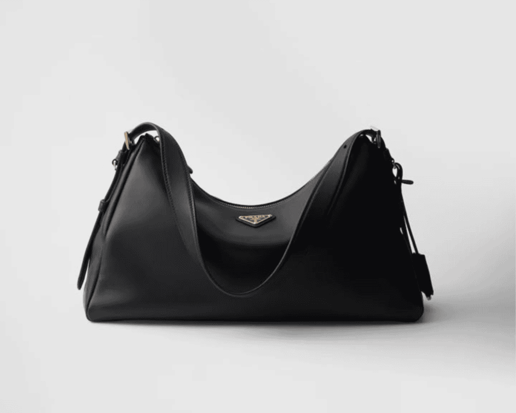 Prada Aimée large shoulder bag in smooth black leather with a slouchy '90s minimalist silhouette, adjustable shoulder strap, and centered enameled metal triangle logo.