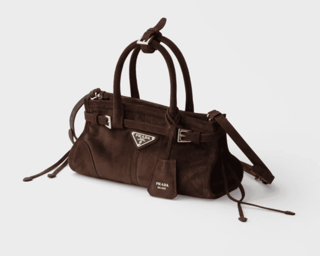Prada Bonnie mini handbag in cacao dark brown soft suede featuring a rectangular silhouette with distinctive metal buckles, side laces, round handles, and an enameled triangle logo.Caption