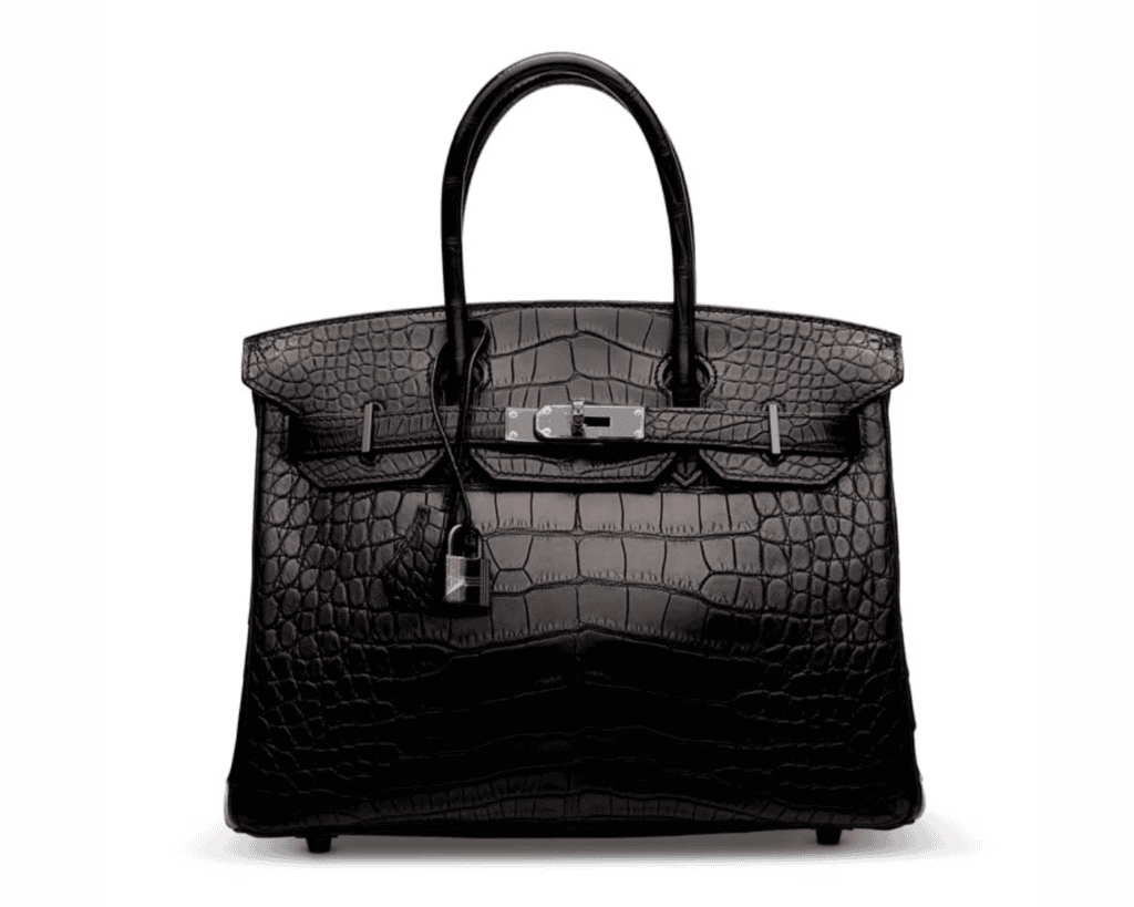 A studio front shot of an ultra-rare, limited edition Hermès Birkin 30 So Black bag crafted from matte Niloticus crocodile skin, showcasing its symmetrical scales, two structured rolled top handles, a matching black PVD-coated turnlock touret closure, and a hanging black leather clochette with a coordinating black padlock.