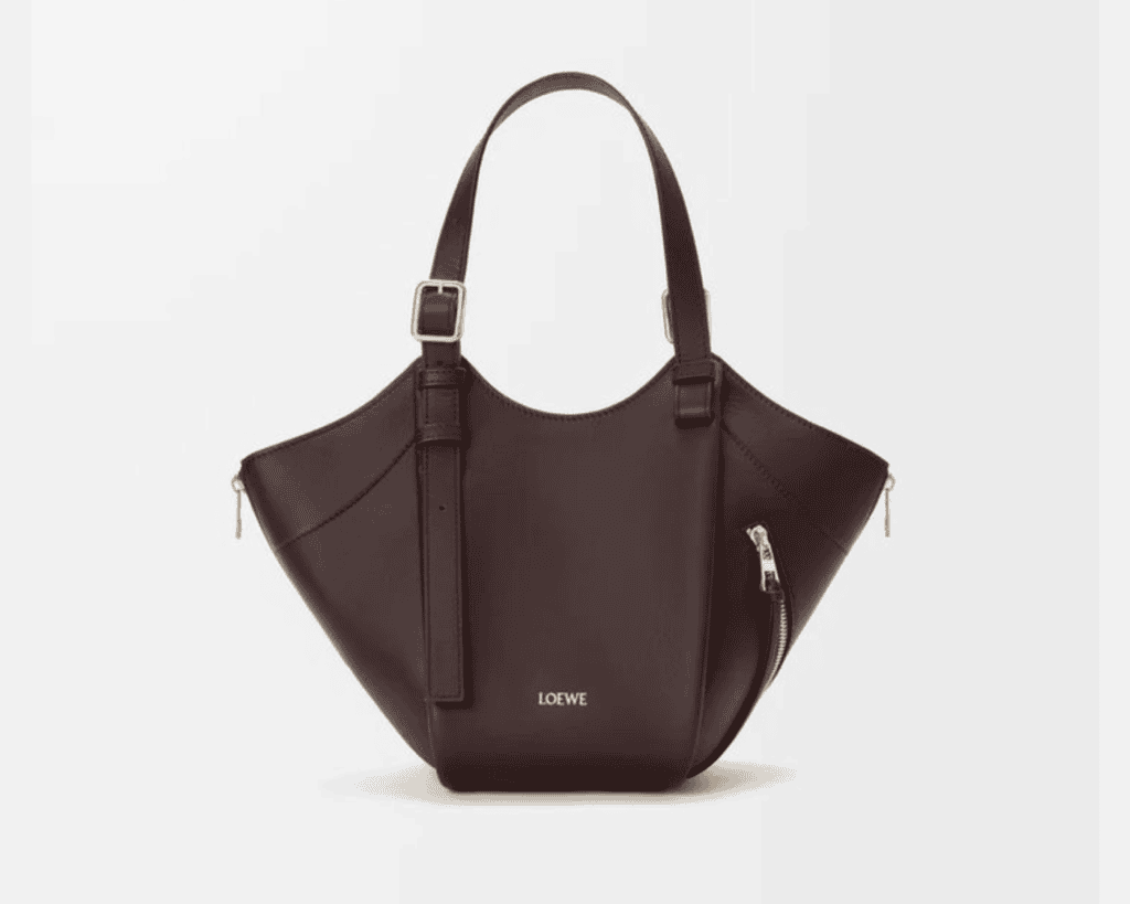 A studio front shot of a dark brown LOEWE Hammock Flip bag made of classic calfskin leather, showcasing its signature origami-inspired folded panels, side zipper detailing, silver-tone buckles on the adjustable flat top handles, and a clean minimalist silver printed logo on the front panel.