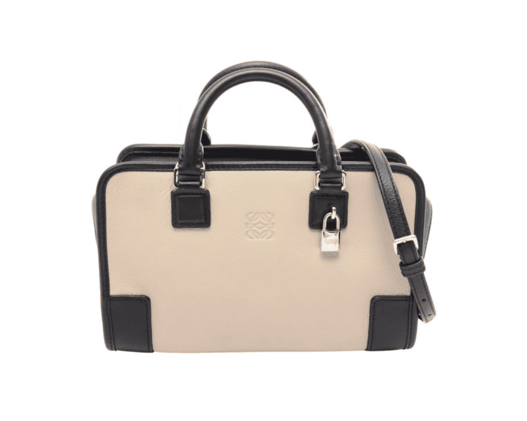 A studio front shot of a rectangular LOEWE Amazona 23 top-handle bag, showcasing a sophisticated beige and black colorblock calfskin leather body with a subtly debossed Anagram logo centered on the cream front panel, two rolled black top handles, a matching slim black shoulder strap, and polished silver-tone palladium padlock details.