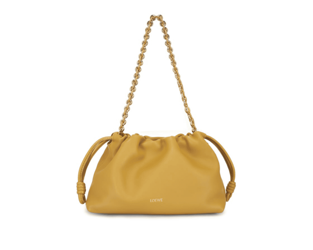 A studio front shot of a mustard-yellow LOEWE Medium Flamenco Purse crafted in supple nappa lambskin leather, featuring its iconic draped dumpling shape with signature side coiled knots, a gold-tone woven leather donut chain handle, and a minimalist gold foil logo printed at the bottom center.