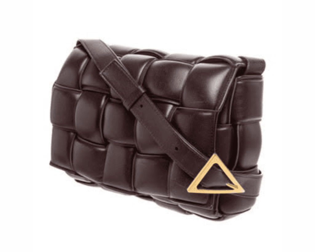 A side-angle studio shot of a dark brown Bottega Veneta Padded Cassette bag, showcasing its puffy, oversized Intrecciato woven leather panels and an adjustable leather shoulder strap fastened with a signature triangular gold-tone buckle.