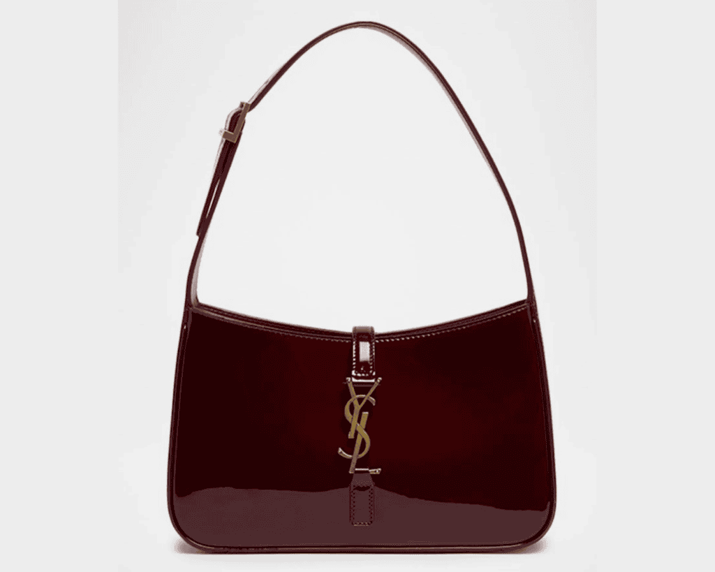 A deep burgundy-red patent leather Saint Laurent Le 5 à 7 shoulder bag Mytheresa with a curved, crescent silhouette Net-a-Porter, featuring an adjustable leather top handle and a central tab closure finished with a gold-tone interlocking YSL Cassandre logo Farfetch, Mytheresa.